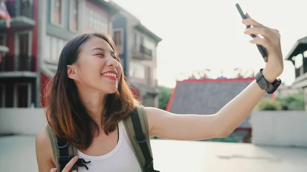 Munter, vakker ung asiatisk backpacker-blogger som bruker smarttelefon som tar selfie mens hun reiser i Chinatown i Beijing, Kina. Livsstilsryggsekkturismebegrepet feriereise . – stockfoto