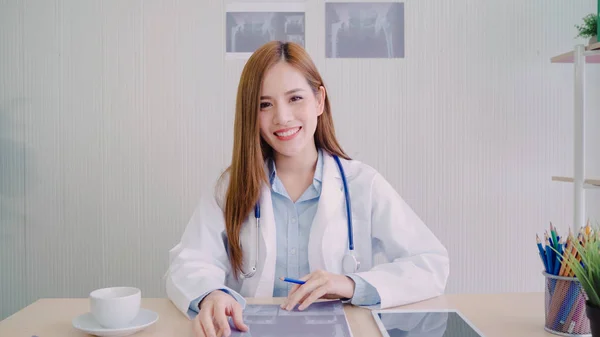 Médica asiática confiante sentada na mesa de escritório e sorrindo para a câmera, cuidados de saúde e conceito de prevenção no consultório médico . — Fotografia de Stock