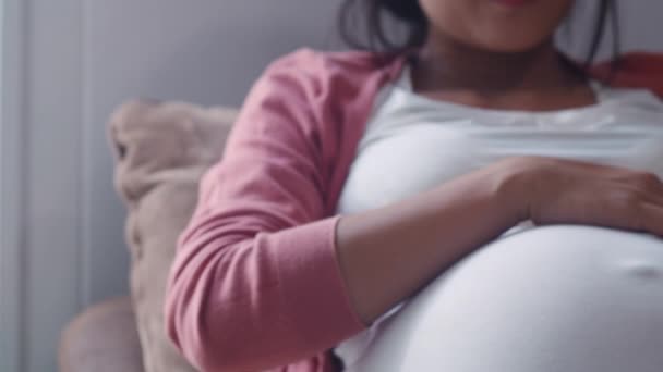 彼女の腹を抱えた若いアジアの妊婦が子供と話している 幸せな笑顔を感じる肯定的で平和なケア赤ちゃん 自宅のコンセプトでリビングルームでソファに横たわっている妊娠 スローモーション — ストック動画