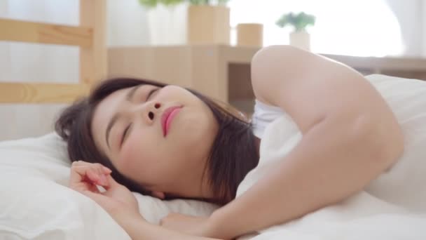 寝室のベッドに横たわって微笑むアジアの女性 自宅で起きた後のリラックスした時間を使用して美しい日本人女性 自宅のコンセプトでリラックスした時間を使用するライフスタイル女性 スローモーションショット — ストック動画