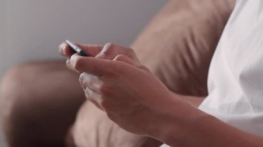 Genç Asyalı adam cep telefonu kullanıyor oturma odasında televizyon oyunu oynuyor, erkek kendini mutlu hissediyor evdeki kanepede uzanmış dinlenme zamanını kullanıyor. Erkekler ev kavramında oyun oynar rahatlar..
