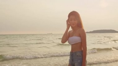 Kum sahilinde koşan Asyalı bir kadın. Bikini li genç mutlu kadın, tatil, tatil, yaz gezisi konsepti, tatil, tatil, yaz gezisi konsepti, gün batımı sırasında tropikal deniz kenarında eğlenceli bir şekilde koşar. Yavaş çekim çekimi.