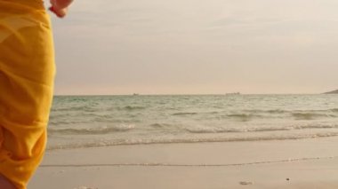 Kum sahilinde koşan Asyalı bir kadın. Bikini li genç mutlu kadın, tatil, tatil, yaz gezisi konsepti, tatil, tatil, yaz gezisi konsepti, gün batımı sırasında tropikal deniz kenarında eğlenceli bir şekilde koşar. Yavaş çekim çekimi.