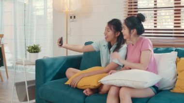 Lezbiyen lgbtq kadın influencer çift evde vlog. Asya sevgilisi kadın mutlu dinlenmek eğlenceli sosyal medyada teknoloji cep telefonu kayıt vlog video upload kullanarak oturma odası kavramı kanepe yatarken.