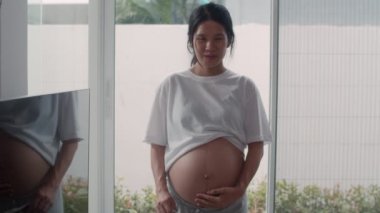 Genç Asya Hamile kadınlar göstermek ve göbek ultrason fotoğraf bebek arıyorum. Anne mutlu gülümseyerek huzurlu hissederken evde ki oturma odasında pencerenin yanında yatan çocuğa özen gösteriyor konsept. Yavaş çekim.