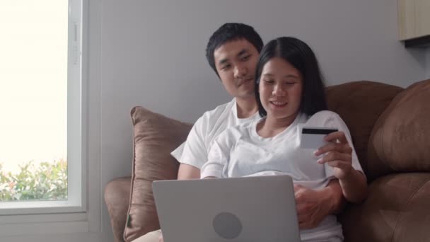 年轻的亚洲怀孕夫妇在家网上购物 妈妈和爸爸在家里客厅的桌子上躺着 用笔记本电脑技术和信用卡购买婴儿用品感到很高兴 慢动作 — 图库视频影像