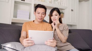 Evdeki oturma odasında internet alışverişi için tablet kullanan Asyalı çift, evde dinlenirken kanepede uzanırken aşk anının tadını çıkarıyor. Yaşam tarzı çifti ev kavramında rahatlar..