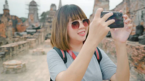Reisende asiatisk kvinne som bruker smarttelefon for å ta et bilde mens hun tilbringer ferieturen på Ayutthaya, Thailand, liker å reise på en fantastisk landemerke i tradisjonell by . – stockfoto