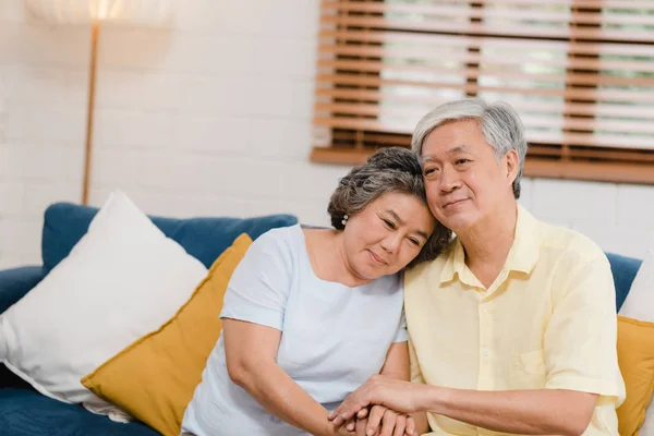 Ein älteres asiatisches Paar hält sich im Wohnzimmer an den Händen, ein Paar, das sich glücklich teilt und sich gegenseitig unterstützt, wenn es zu Hause auf dem Sofa liegt. Lifestyle Seniorenfamilie zu Hause Konzept. — Stockfoto