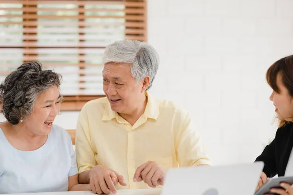 Asia agente femenino inteligente ofrece seguro de salud para parejas de ancianos por documento, tableta y computadora portátil. Envejecido asiático pareja consultando con el agente de seguros mientras se sienta junto con en casa . — Foto de Stock