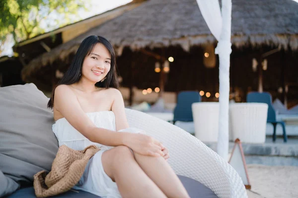 Mujer asiática joven sentada en el banco relajarse en la playa, hermosa mujer feliz relajarse cerca del mar. Estilo de vida de las mujeres viajan en concepto de playa . —  Fotos de Stock