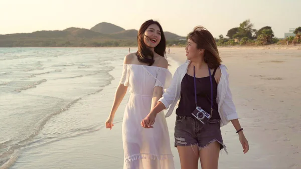 Young Asian lesbian couple walking on beach. Beautiful women friends happy relax walking on beach near sea when sunset in evening. Lifestyle lesbian couple travel on beach concept.