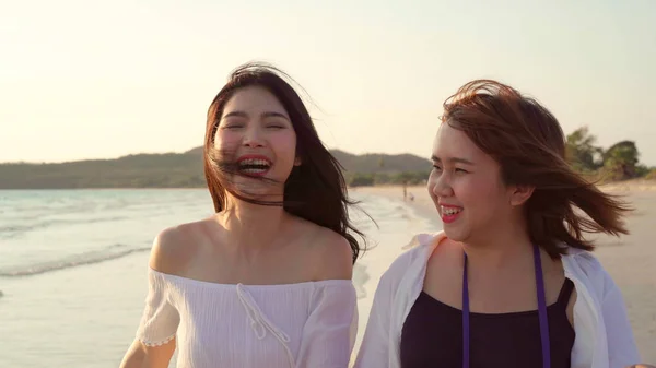 Giovane coppia lesbica asiatica a piedi sulla spiaggia. Belle amiche donne felici rilassarsi passeggiando sulla spiaggia vicino al mare quando il tramonto in serata. Stile di vita coppia lesbica viaggiare sul concetto di spiaggia . — Foto Stock