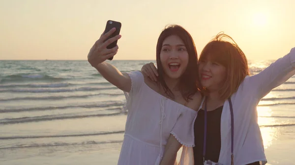 Junges asiatisches lesbisches Paar mit Smartphone, das Selfie in Strandnähe macht. schöne Frauen lgbt Paar glücklich entspannen genießen Liebe Moment, wenn Sonnenuntergang am Abend. Lifestyle lesbisches Paar reist am Strand Konzept — Stockfoto