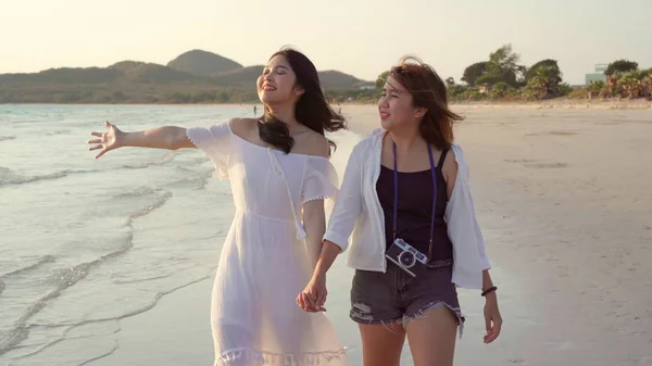 Giovane coppia lesbica asiatica a piedi sulla spiaggia. Belle amiche donne felici rilassarsi passeggiando sulla spiaggia vicino al mare quando il tramonto in serata. Stile di vita coppia lesbica viaggiare sul concetto di spiaggia . — Foto Stock