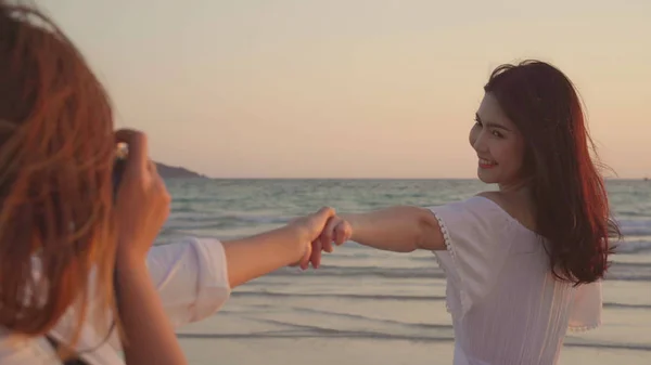 Joven asiática lesbiana pareja usando cámara tomando fotos unos a otros cerca de la playa. Hermosas mujeres lgbt pareja feliz momento romántico al atardecer en la noche. Estilo de vida lesbiana pareja viajar en playa concepto . —  Fotos de Stock
