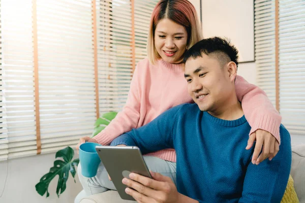 Atraente casal doce asiático usando tablet enquanto deitado no sofá quando relaxar em sua sala de estar em casa. Marido e sua esposa usando relaxar e tempo romântico em casa conceito . — Fotografia de Stock