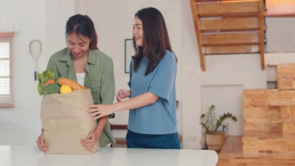 亚洲女同性恋Lgbtq女夫妇拿着杂货店购物纸袋在家里 年轻的亚洲女孩快乐购买蔬菜和水果健康产品从超市把它放在厨房在早上的概念 — 图库视频影像