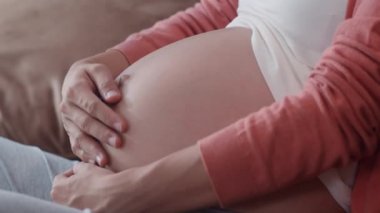 Genç Asyalı hamile kadın karnını tutuyor ve çocuğuyla konuşuyor. Annem mutlu, pozitif ve huzurlu gülümserken kendine iyi bak bebeğim. Oturma odasındaki kanepede uzanmış hamilelik..