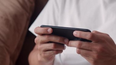 Genç Asyalı adam cep telefonu kullanıyor oturma odasında televizyon oyunu oynuyor, erkek kendini mutlu hissediyor evdeki kanepede uzanmış dinlenme zamanını kullanıyor. Erkekler ev kavramında oyun oynar rahatlar..