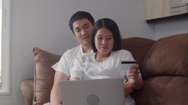 年轻的亚洲怀孕夫妇在家里网上购物 爸爸妈妈很高兴用笔记本电脑和信用卡购买婴儿用品 而在客厅的沙发上躺着在家的概念 — 图库视频影像