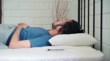 Genç Asyalı bir adam sabah uyandığında, Asyalı bir erkek evdeki yatak odasında uyandıktan sonra cep telefonunun alarmını kapatıyor. Yakışıklı erkekler uyur, uyur. Modern ev konseptinde rahatlarlar..