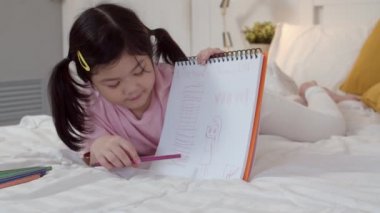 Genç Asyalı kız evde çizim. Asya japon kadın çocuk çocuk dinlenmek eğlenceli gece konsepti yatak odasında yatak odasında uyku, konfor ve sakin yatmadan önce sketchbook karikatür çizin. Yavaş çekim.