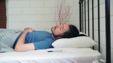 Genç Asyalı bir adam sabah uyandığında, Asyalı bir erkek evdeki yatak odasında uyandıktan sonra cep telefonunun alarmını kapatıyor. Yakışıklı erkekler uyur, uyur. Modern ev konseptinde rahatlarlar..