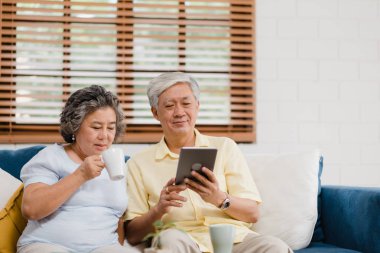 Tablet kullanma ve içme kahve evde oturma odasında Asya yaşlı çift çift evde rahat zaman kanepede yatarken aşk anın tadını çıkarın. Zaman yaşam tarzı üst düzey aile ev concept, zevk.