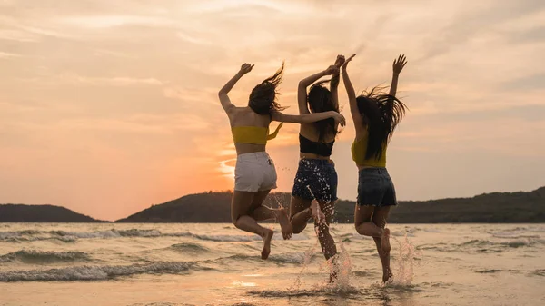 Grupo de três jovens mulheres asiáticas pulando na praia, amigos felizes relaxar se divertindo brincando na praia perto do mar quando o sol se põe à noite. Estilo de vida amigos viagem férias na praia verão conceito . — Fotografia de Stock