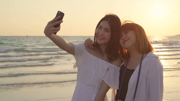 Giovane coppia lesbica asiatica utilizzando smartphone prendere selfie vicino alla spiaggia. Belle donne lgbt coppia felice relax godere momento d'amore quando il tramonto in serata. Stile di vita coppia lesbica viaggiare sul concetto di spiaggia — Foto Stock