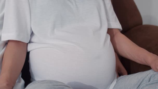 年轻的亚洲怀孕夫妇做心标志抱着肚子 爸爸妈妈开心地开心地微笑着一边照顾宝宝 怀孕时躺在家里的客厅里的桌子上 慢动作 — 图库视频影像