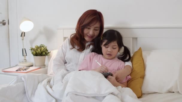 タブレットを使用してアジアの祖母は 自宅で孫娘におとぎ話を読みます シニア中国人 おばあちゃんは 夜の概念で自宅の寝室でベッドに横たわって就寝前に若い女の子をリラックス スローモーション — ストック動画