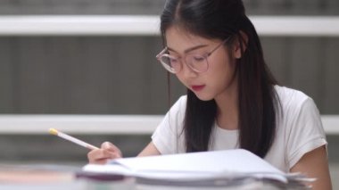 Asyalı öğrenci kadınlar üniversitede kütüphanede kitap okuyor. Genç lisans kız ev ödevi yapmak, ders kitabı okumak, üniversite kampüsünde ders masasında bilgi ve eğitim için çok çalışmak. Yavaş çekim.