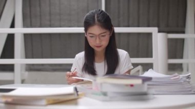 Asyalı öğrenci kadınlar üniversitede kütüphanede kitap okuyor. Genç lisans kız ev ödevi yapmak, ders kitabı okumak, üniversite kampüsünde ders masasında bilgi ve eğitim için çok çalışmak. Yavaş çekim.