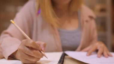 Asyalı öğrenci kadınlar üniversitede kütüphanede kitap okuyor. Genç lisans kız ev ödevi yapmak, ders kitabı okumak, üniversite kampüsünde ders masasında bilgi için çok çalışmak fazla mesai gece. Yavaş çekim.