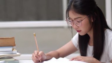 Asyalı öğrenci kadınlar üniversitede kütüphanede kitap okuyor. Genç lisans kız ev ödevi yapmak, ders kitabı okumak, üniversite kampüsünde ders masasında bilgi ve eğitim için çok çalışmak. Yavaş çekim.