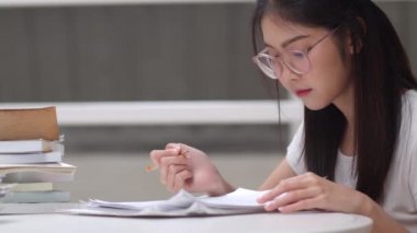Asyalı öğrenci kadınlar üniversitede kütüphanede kitap okuyor. Genç lisans kız ev ödevi yapmak, ders kitabı okumak, üniversite kampüsünde ders masasında bilgi ve eğitim için çok çalışmak. Yavaş çekim.