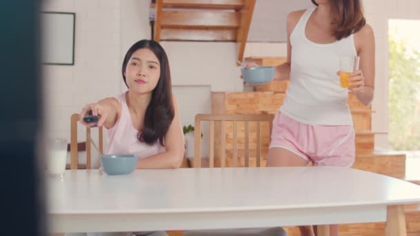 アジアのレズビアンLgbtq女性カップルは自宅で朝食を持っている 若いアジアの恋人の女の子は 朝のコンセプトで台所のテーブルの上にジュース トウモロコシフレークシリアルとミルクを飲みながらテレビを見て幸せ — ストック動画