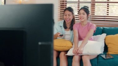 Genç Asya Lezbiyen lgbtq kadın çift evde Tv izlerken, Asyalı sevgilisi kadın duygu mutlu eğlenceli gülmek görünümlü televizyon dizisi film birlikte evde oturma odasında kanepeydeyken kavramı.