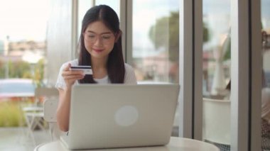 Serbest Asya kadın kahve dükkanında online alışveriş. Genç Asya Kız dizüstü bilgisayar kullanarak, kredi kartı satın almak ve akşam konsepti bir açık hava kafede masada internet üzerinden e-ticaret satın. Yavaş çekim