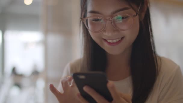 オフィスで携帯電話を使用するフリーランスのアジアの女性 職場のコンセプトでテーブルの上にインターネット上のソーシャルメディアをチェックするスマートフォンを使用して若い日本のアジアの女の子 スローモーションとクローズアップショット — ストック動画