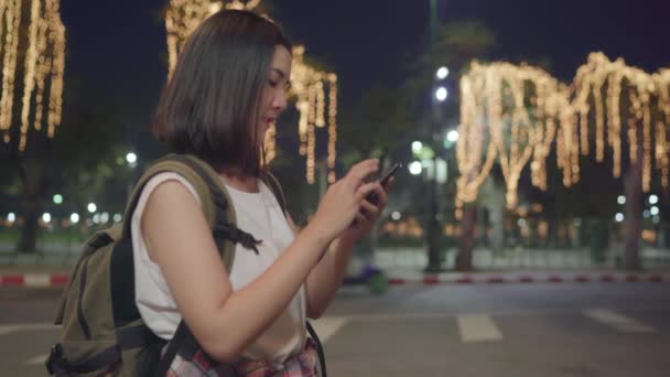 背包客亚洲妇女旅行在曼谷 年轻的亚洲旅游女孩使用手机检查社交媒体在夜间 同时沿着街道散步享受旅程度假旅游概念 — 图库视频影像