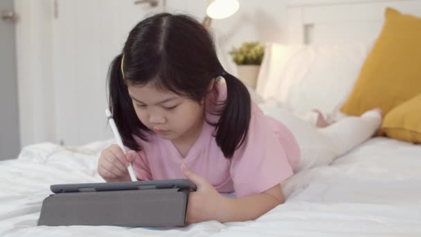 自宅で描く若いアジアの女の子 アジア日本の女性の子供の子供は ベッドに横たわって寝る前にタブレットドロー漫画を使用して幸せにリラックスしてリラックスし 夜のコンセプトで寝室で快適さと落ち着きを感じます スローモーション — ストック動画