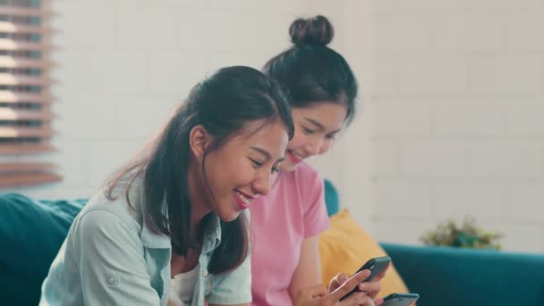若いレズビアンLgbtqアジアの女性カップルは 自宅で携帯電話を使用しています アジアの恋人女性ハッピーは リビングルームのコンセプトでソファを横たわっている間 一緒にインターネットでソーシャルメディアをチェック技術を使用してリラックス楽しい — ストック動画