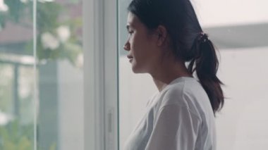 Genç Asya Hamile çift sarılmak ve çocukları ile konuşurken göbek tutarak. Anne ve baba mutlu gülümseyerek huzurlu bir şekilde bakarken bebek, evde oturma odasında pencerenin yanında hamilelik. Yavaş çekim.