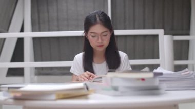 Asyalı öğrenci kadınlar üniversitede kütüphanede kitap okuyor. Genç lisans kız ev ödevi yapmak, ders kitabı okumak, üniversite kampüs kavramı ders masasında bilgi ve eğitim için çok çalışmak.
