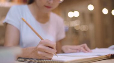 Asyalı öğrenci kadınlar üniversitede kütüphanede kitap okuyor. Genç lisans kız ev ödevi yapmak, ders kitabı okumak, üniversite kampüsünde ders masasında bilgi için çok çalışmak fazla mesai gece. Yavaş çekim.