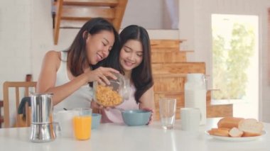 Asya lezbiyen LGBTQ kadınlar çift evde kahvaltı var, Genç Asya sevgilisi kadın duygu mutlu İçecek suyu, Mısır gevreği ve süt mutfakta masada kase sabah kavramı.