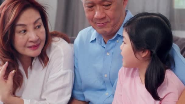 アジアの祖父母が自宅で孫娘と話す シニア中国 古い世代 祖父と祖母の家族の時間は リビングルームのコンセプトでソファの上に若い女の子とリラックス スローモーション — ストック動画